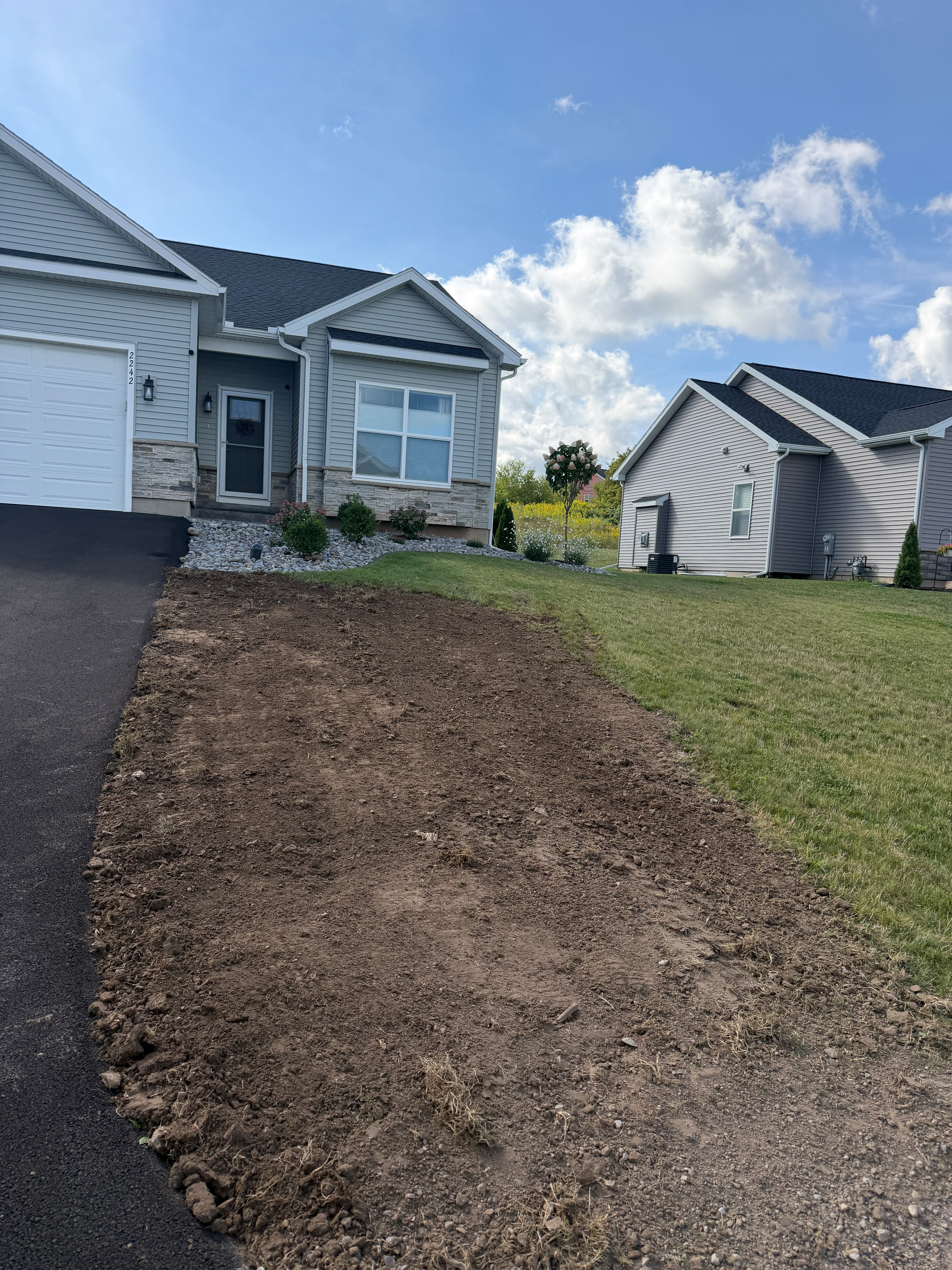 Front yard bed cleared and graded beside a driveway, ready for new landscaping
