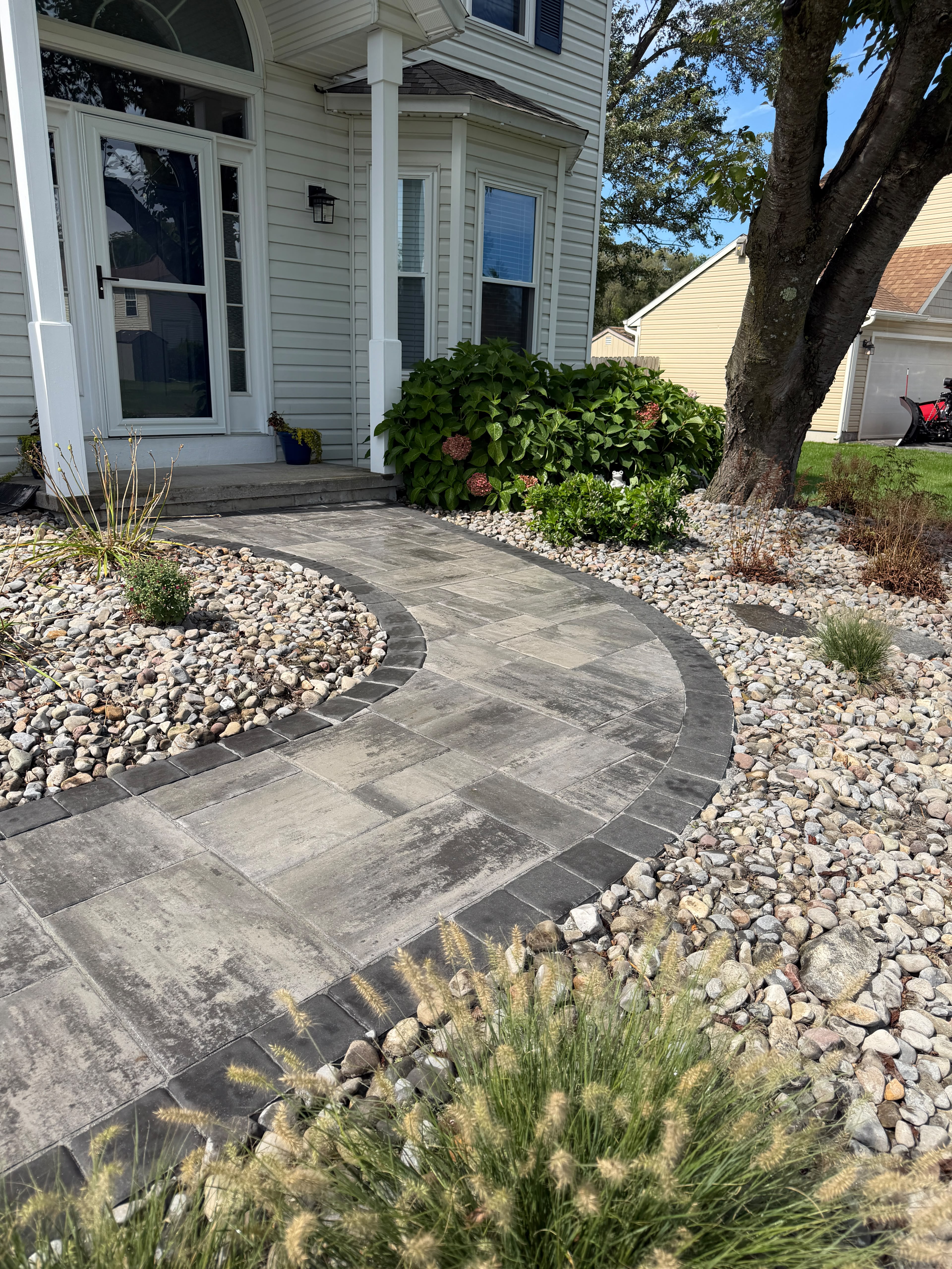 Curved paver walkway with a charcoal border leading to a front door through river rock beds