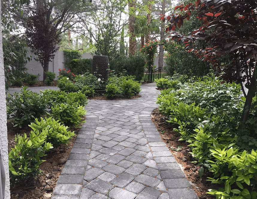 Curved gray stone pathway surrounded by green shrubs and trees in a garden setting.