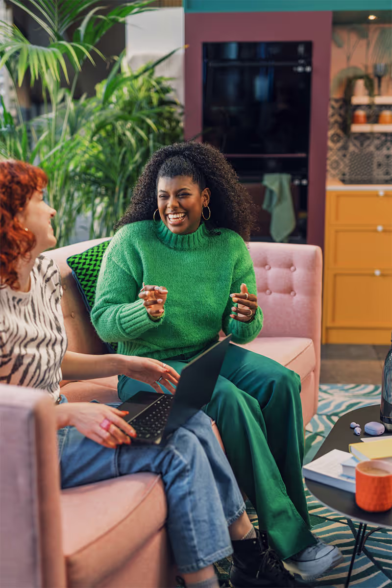 Two women sitting on a couch talking to each other.