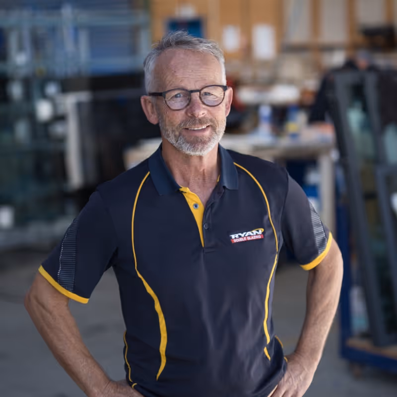 Middle-aged man with glasses and gray hair wearing a Ryan Double Glazing polo shirt, standing indoors with hands on hips.