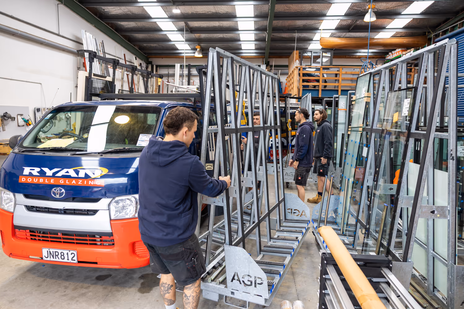 Workers handling large glass panels inside a warehouse with a blue and orange Ryan Double Glazing van parked nearby.
