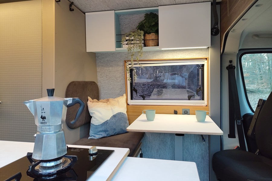 the lounge area of the van with 2 cups of cappuccino on the table and a Bialetti Moka in the foreground