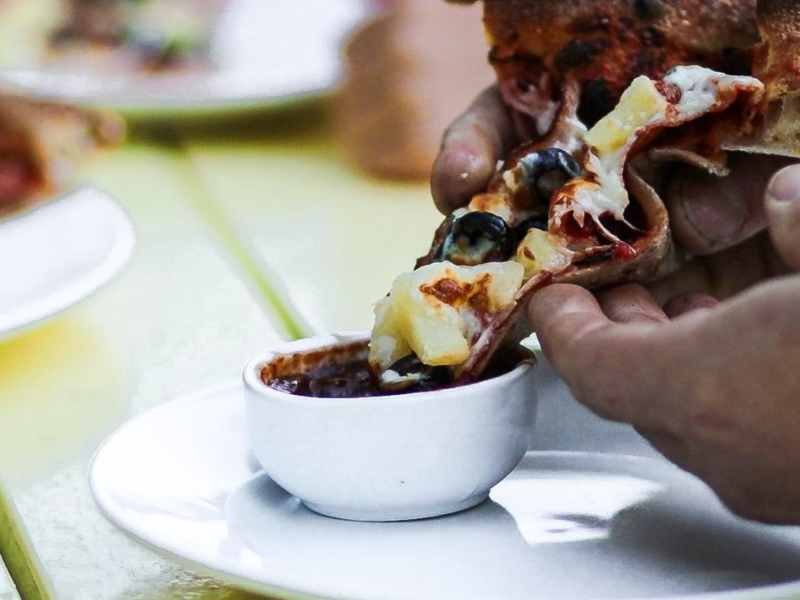 Pizza being dipped in Slow Bottle Sunday sauce.