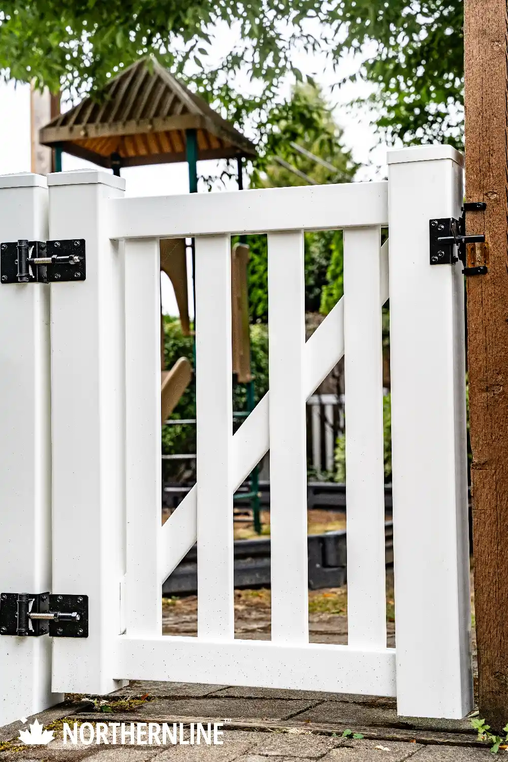 White vinyl gate with diagonal brace and black hinges in an outdoor garden setting.
