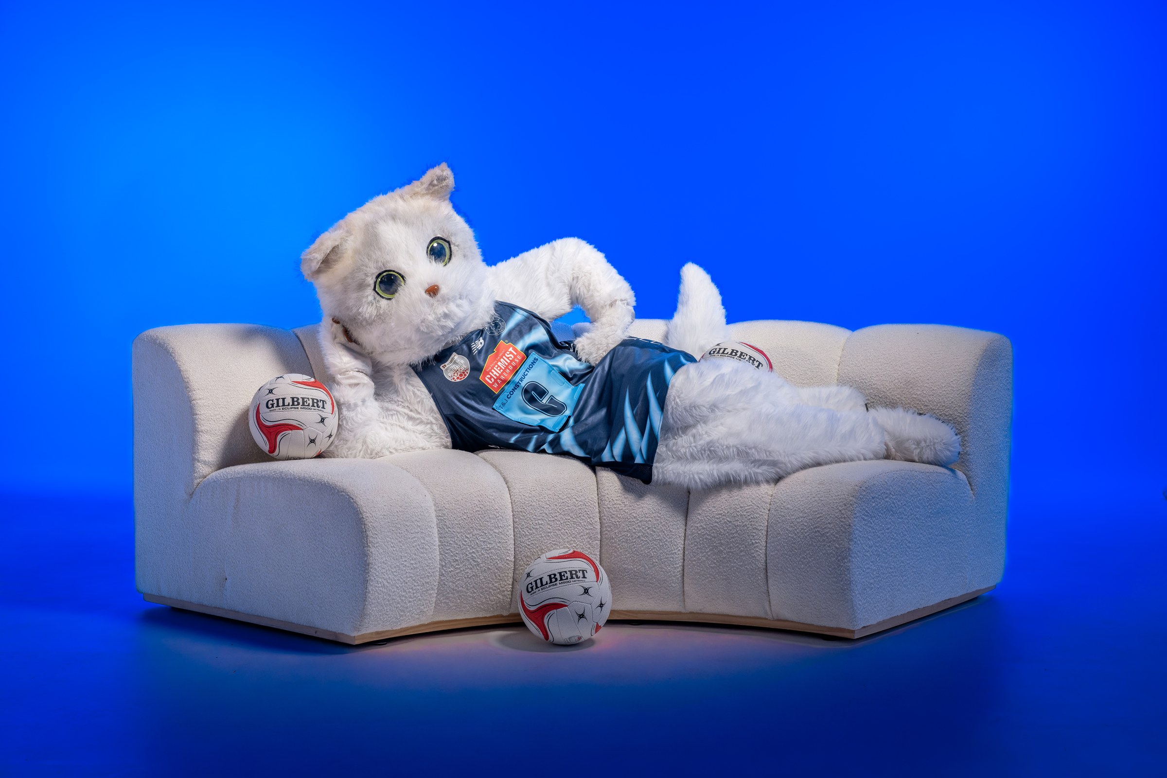 Mishka, the Walkerville club mascot, sitting on a sofa with two netballs
