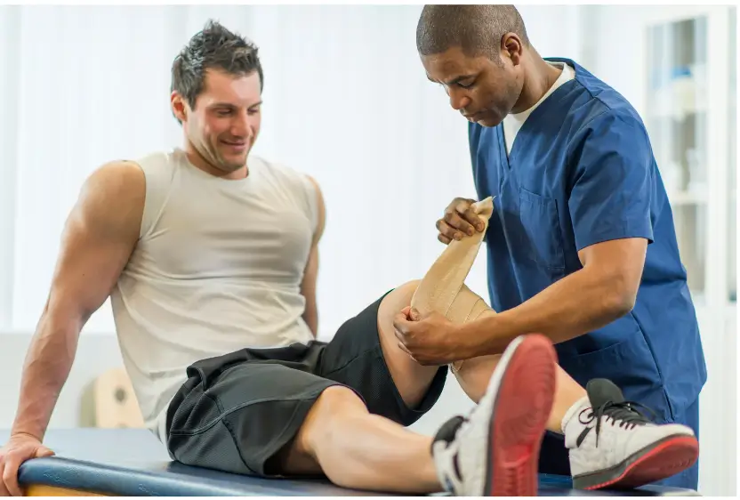 A physical therapist wrapping a man's knee.