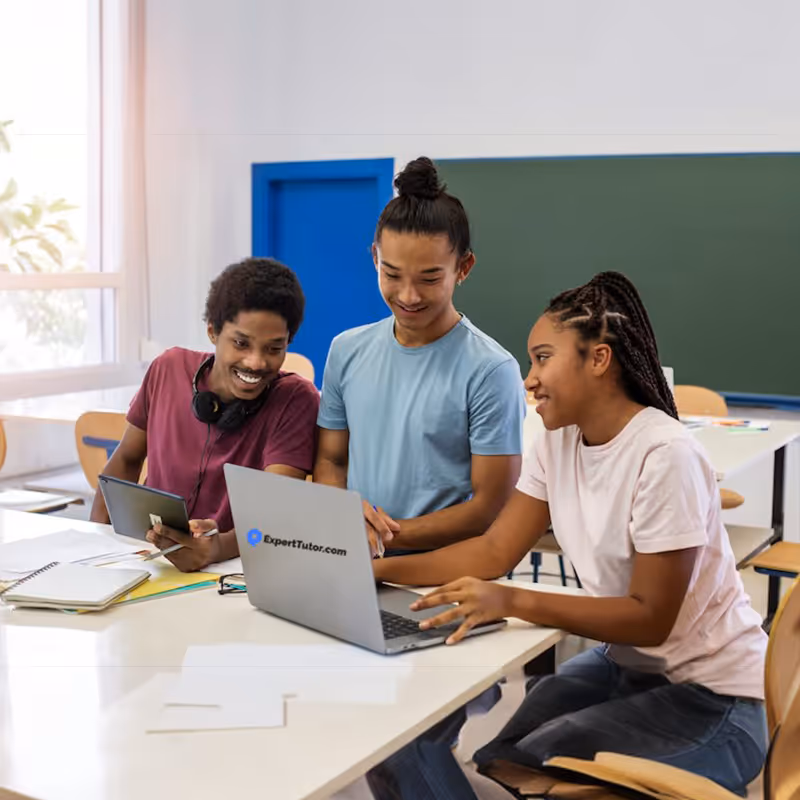 Three students studying together with a laptop and tablet in a classroom.