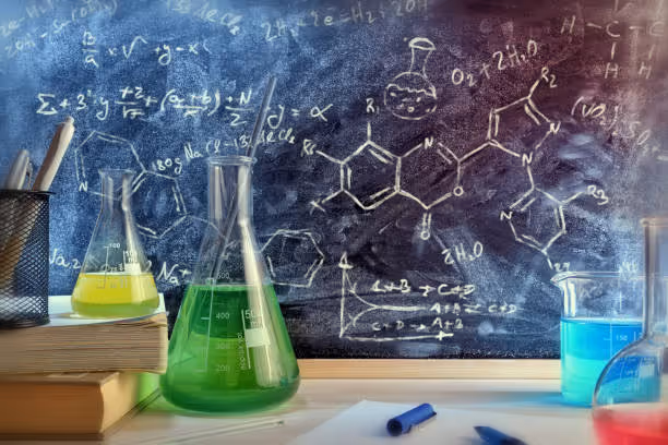 Lab table with colorful chemical solutions in flasks and complex formulas on a chalkboard background.