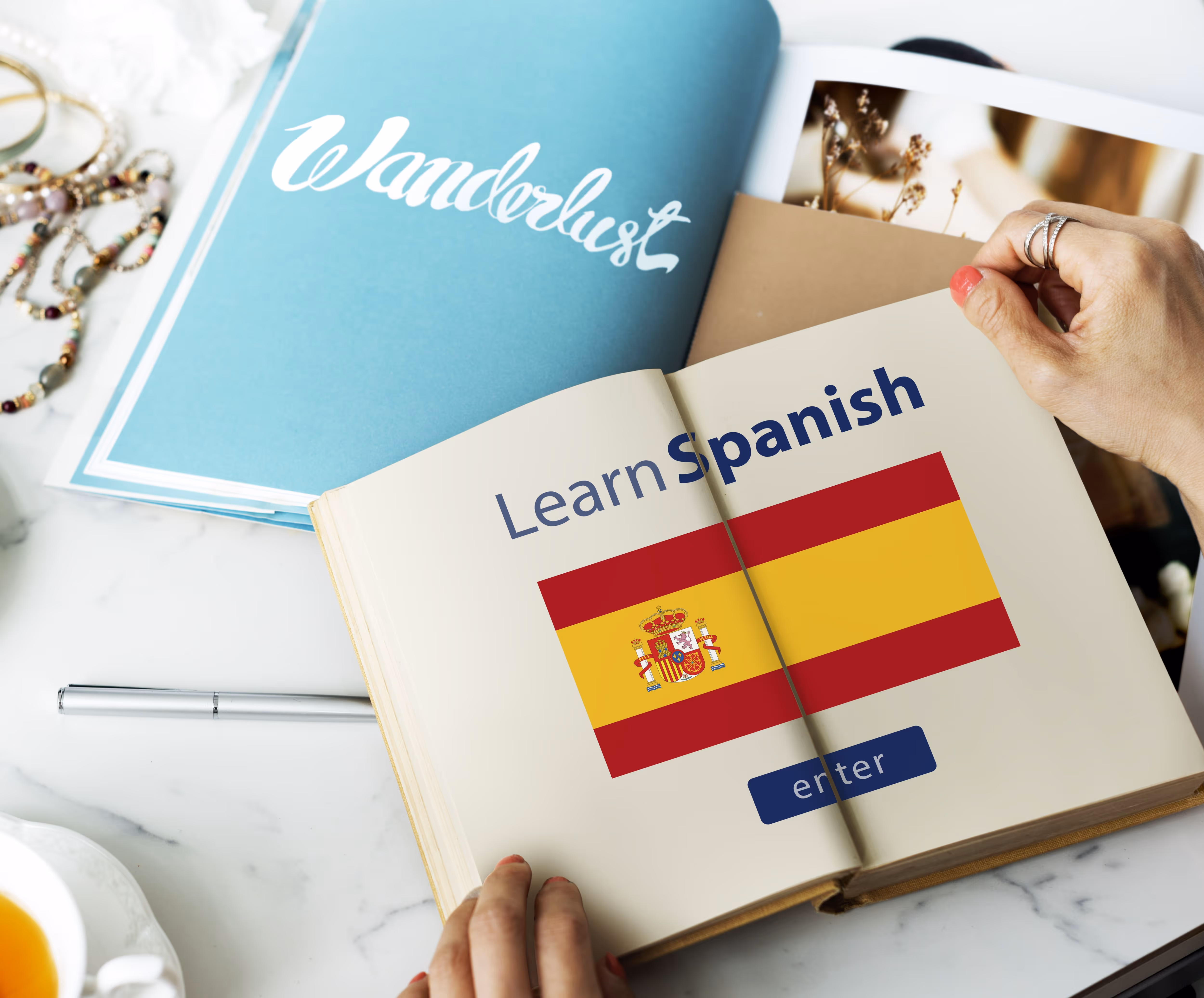 Hands open a book displaying 'Learn Spanish' with a Spanish flag and an 'enter' button graphic.