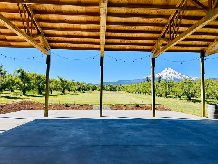 Side view of the open-air wedding pavilion with wine barrels inside, framed by pear orchards in the Hood River Valley.
