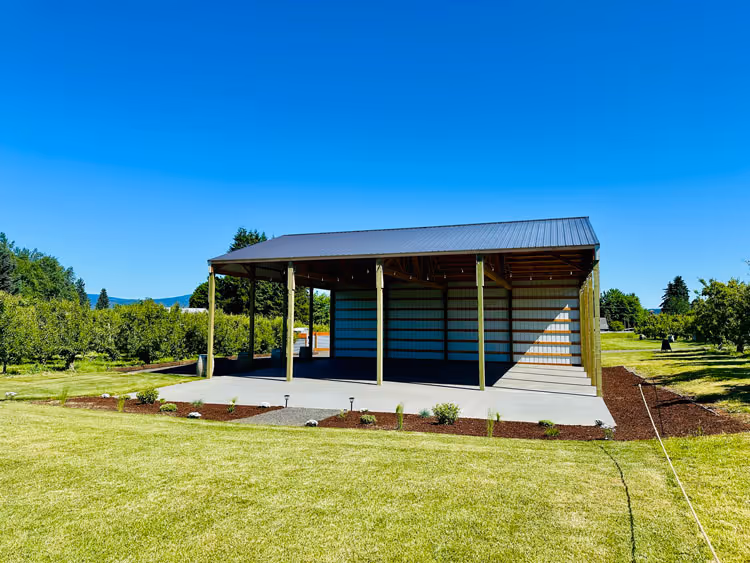 Covered pole barn pavilion with string lights, set within the pear orchard with Mt. Hood in the distance.