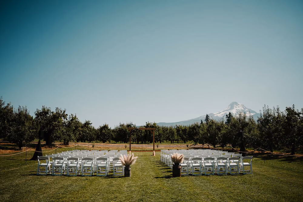 Ceremony setup at The Perfect Pear in Parkdale, Oregon, with white chairs, lush grass lining the aisle, and a wooden arch.