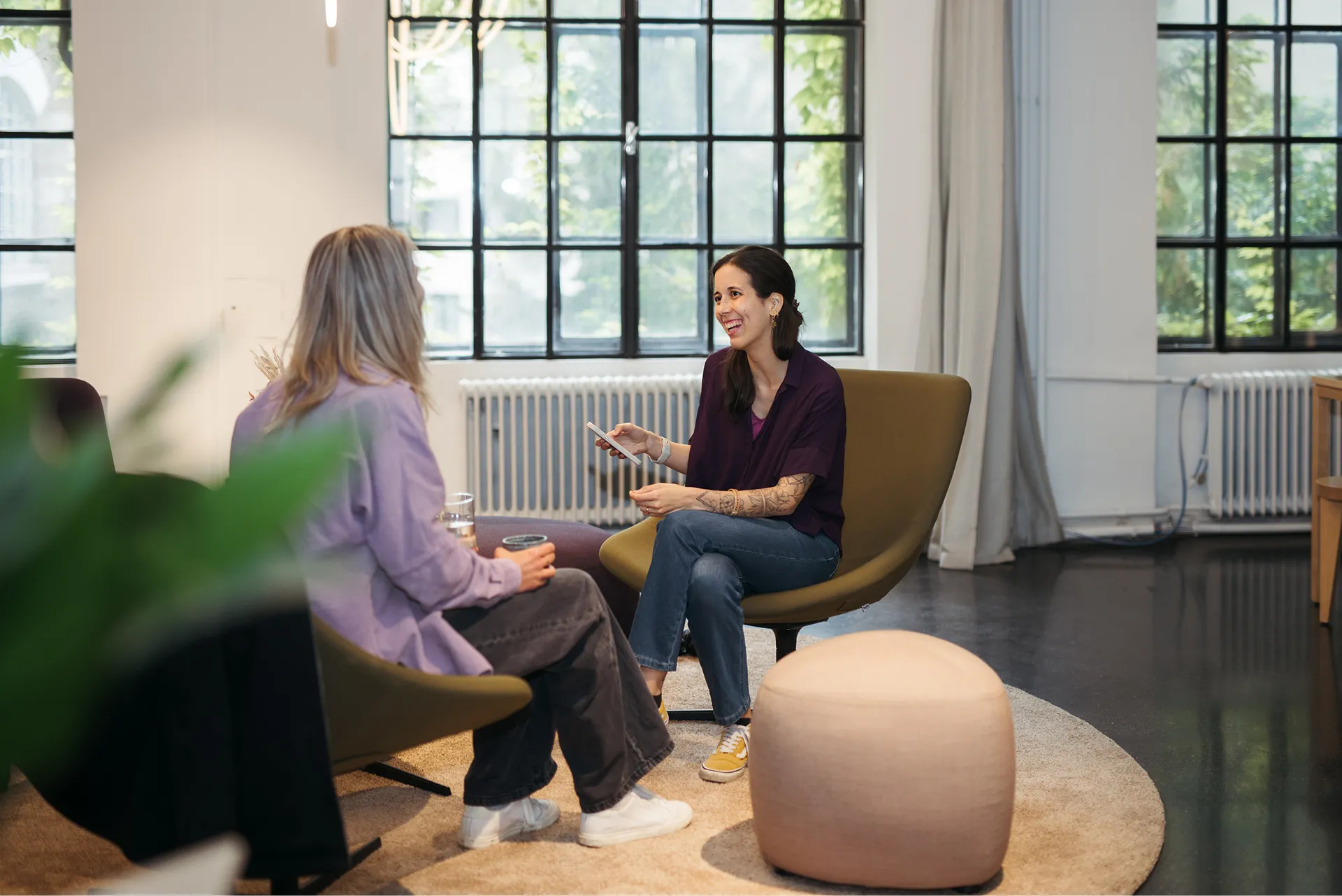 Zwei Frauen sitzen sich in einem modernen Raum auf Sesseln gegenüber und führen ein freundliches Gespräch.