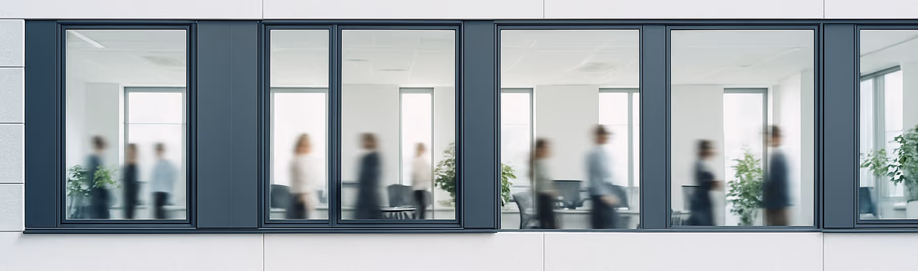Verschwommene Silhouetten von Personen, die sich in einem modernen Büro mit großen Fenstern bewegen.