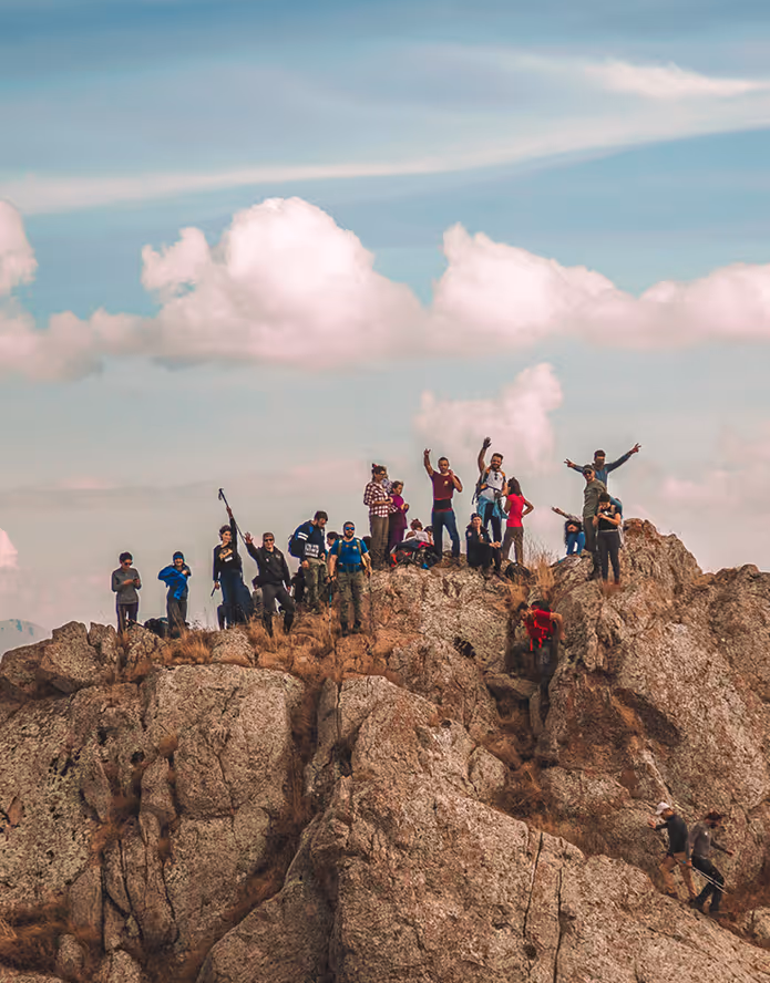 Gruppe von Wanderern steht auf einem felsigen Berggipfel unter blauem Himmel mit Wolken.
