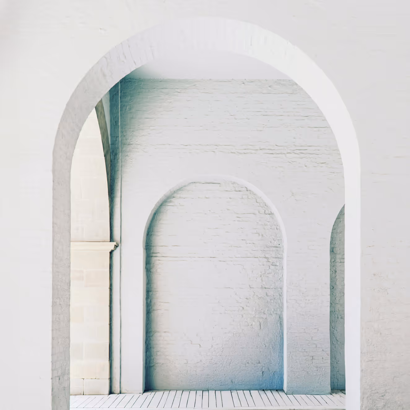 Weiße Ziegelwand mit drei rechteckigen Bogenöffnung in einem minimalistischen Raum.