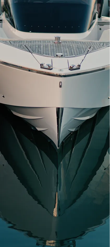 Close-up of a white yacht's pointed bow reflecting on calm water.