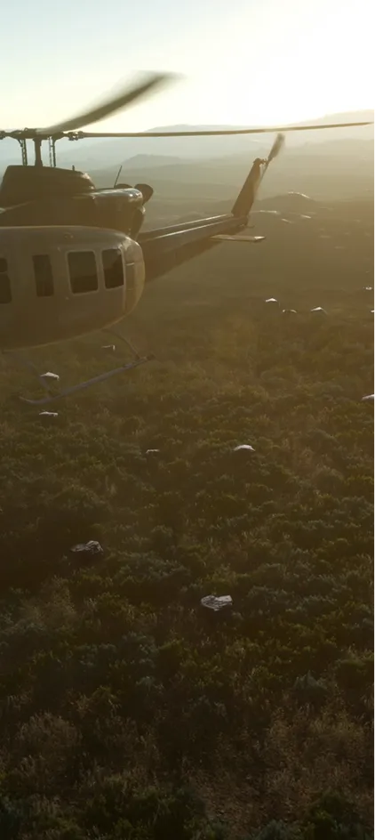 Helicopter flying over forested landscape at sunset with rotor blades in motion.