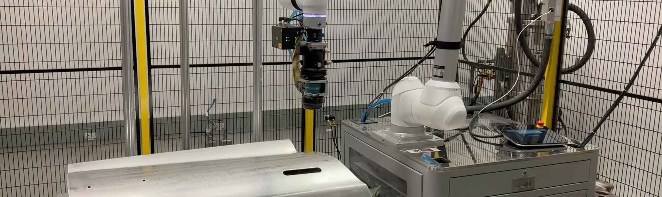 Robotic arm system inside safety cage working with metal parts on a factory floor.