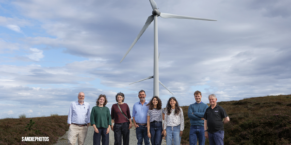 A group of people standing in front of a wind farm