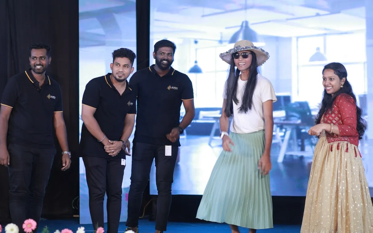 A grayscale image of three men engaged in a professional discussion within a modern open-plan office.