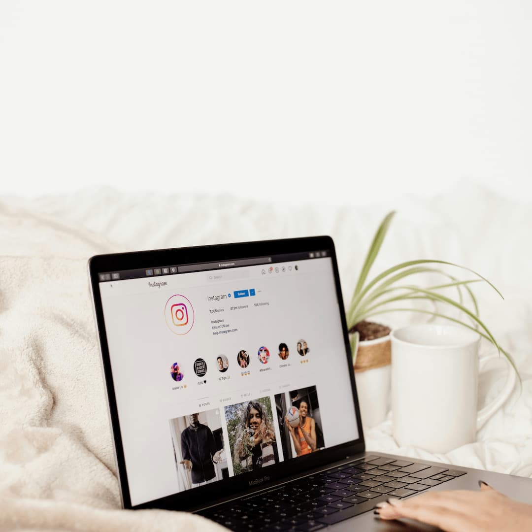 Personne utilisant un MacBook Pro affichant la page Instagram officielle, avec une tasse blanche et une plante en arrière-plan.
