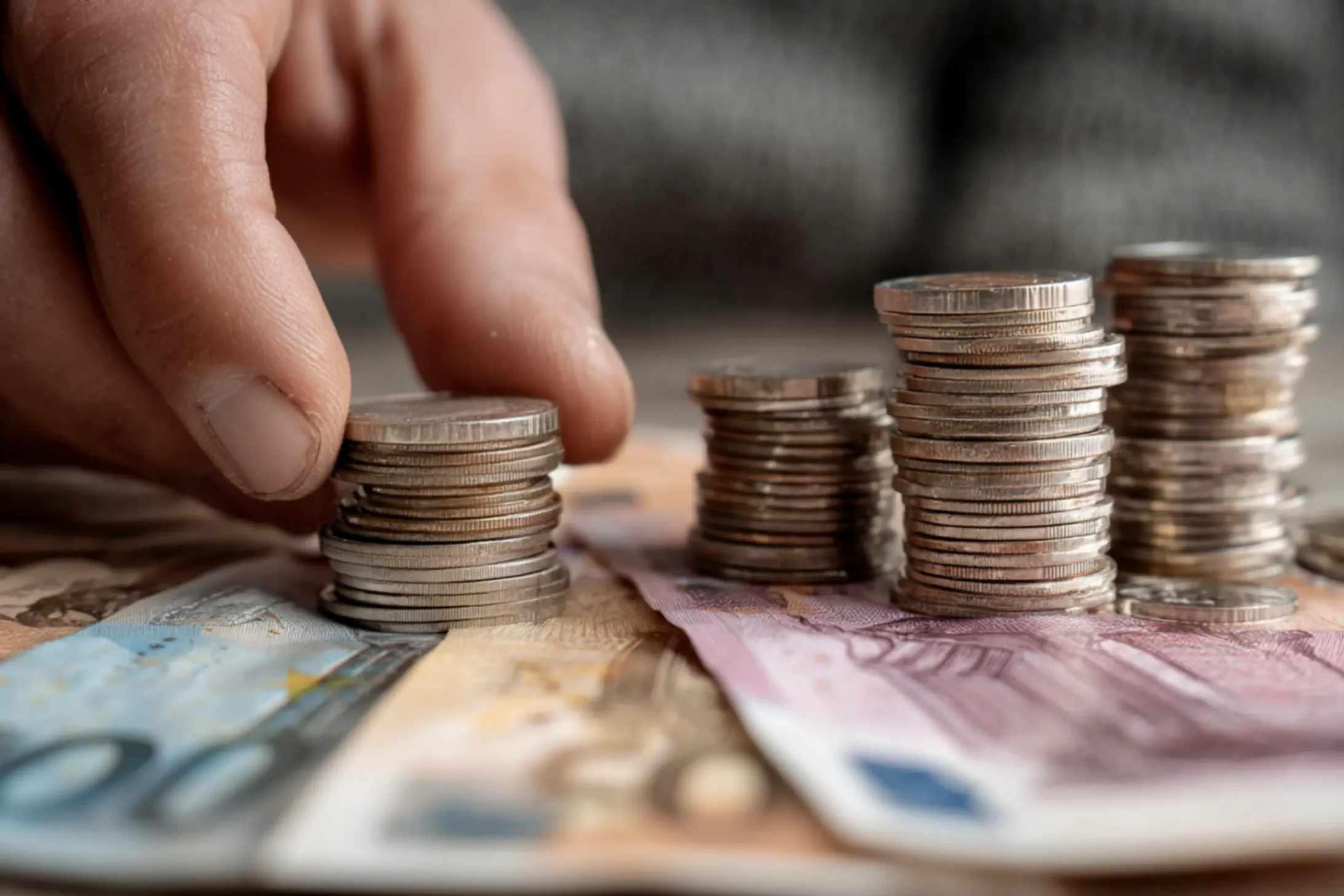un zoom sur une pile de monnaie avec des billets placés sur la table et une main qui compte l'argent