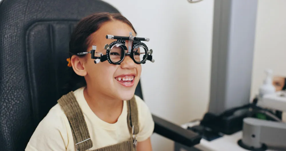 Smiling young girl wearing an eye exam trial frame during an eye test.