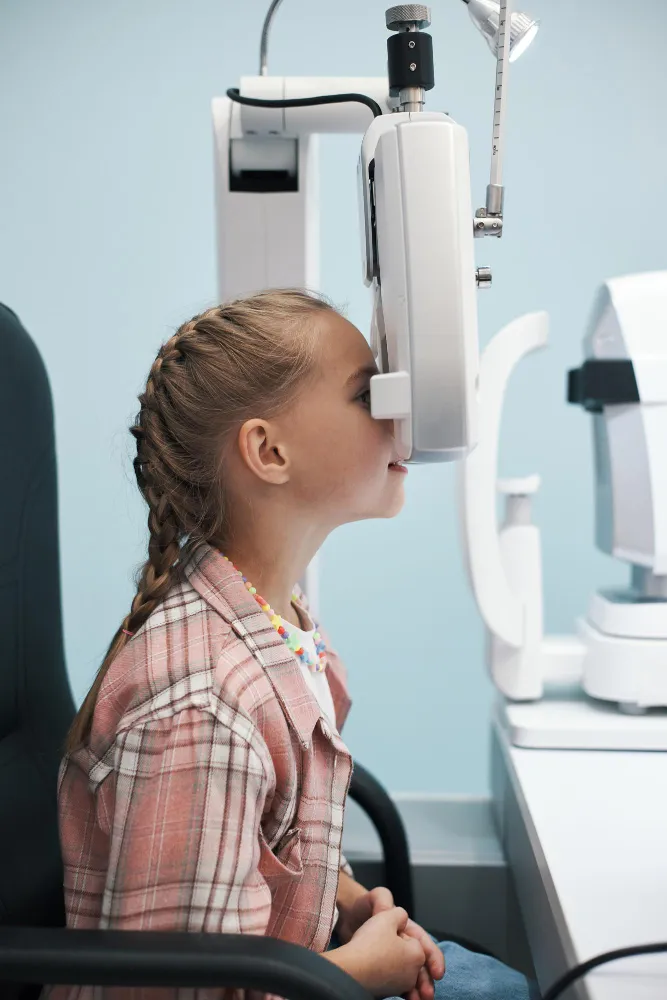 Young girl undergoing an eye exam using an optical eye testing machine at a clinic.