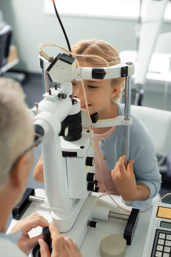 Young girl undergoing an eye exam with an optometrist using a slit lamp microscope.