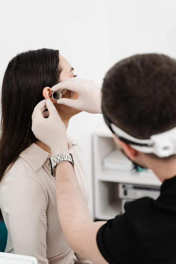 Medical professional wearing gloves using otoscope to examine a woman's ear in a clinic.