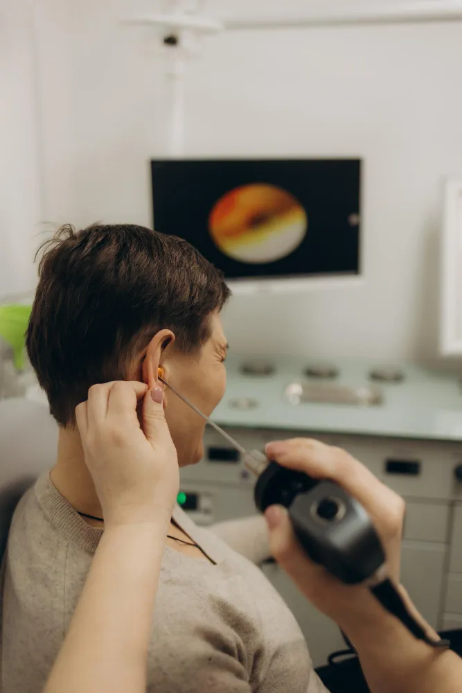 Person having ear examined with an otoscope by a healthcare professional in a medical setting.