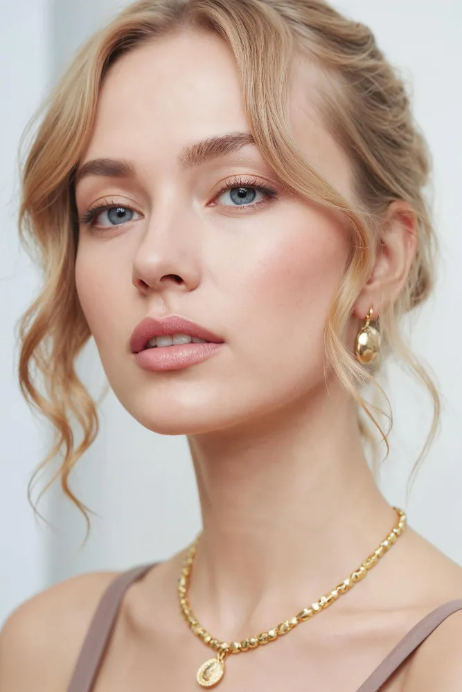 Close-up of a young woman with blonde hair, blue eyes, wearing gold necklace and matching earrings.