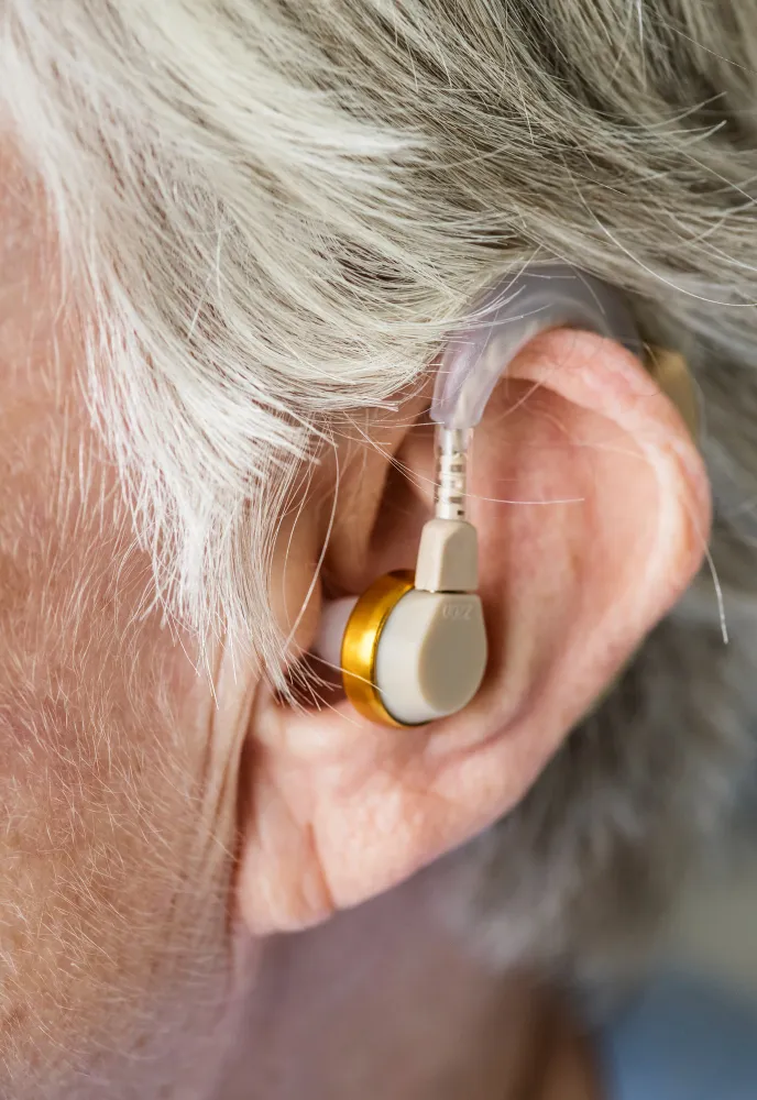 Close-up of an elderly person's ear with a hearing aid device inserted.
