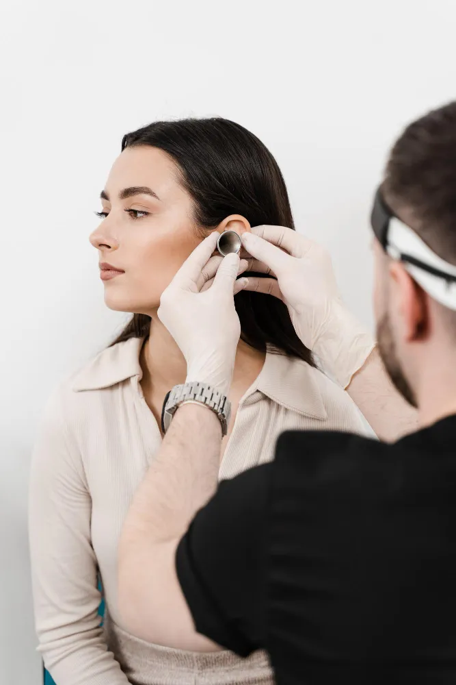 Woman receiving ear examination by a healthcare professional wearing gloves using an otoscope.