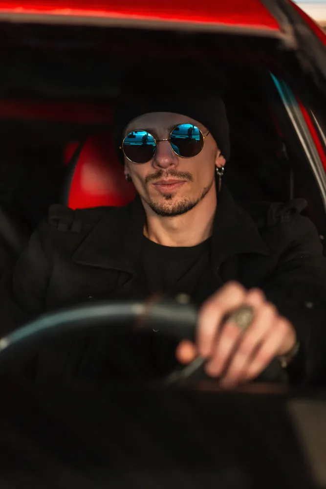 Man wearing black beanie and sunglasses driving a car with red interior.