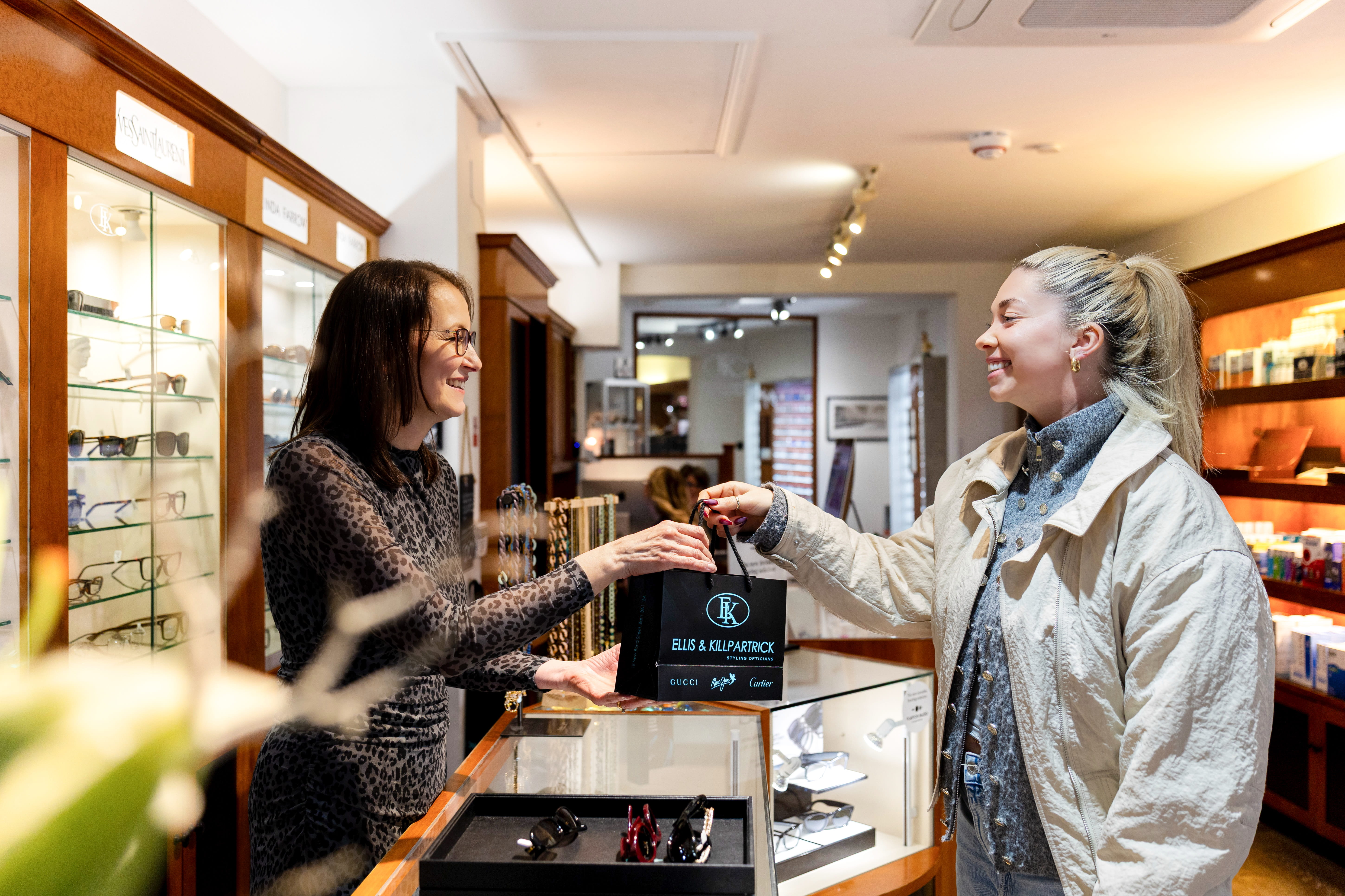Woman customer receiving a shopping bag at an eyewear store counter with display of glasses.