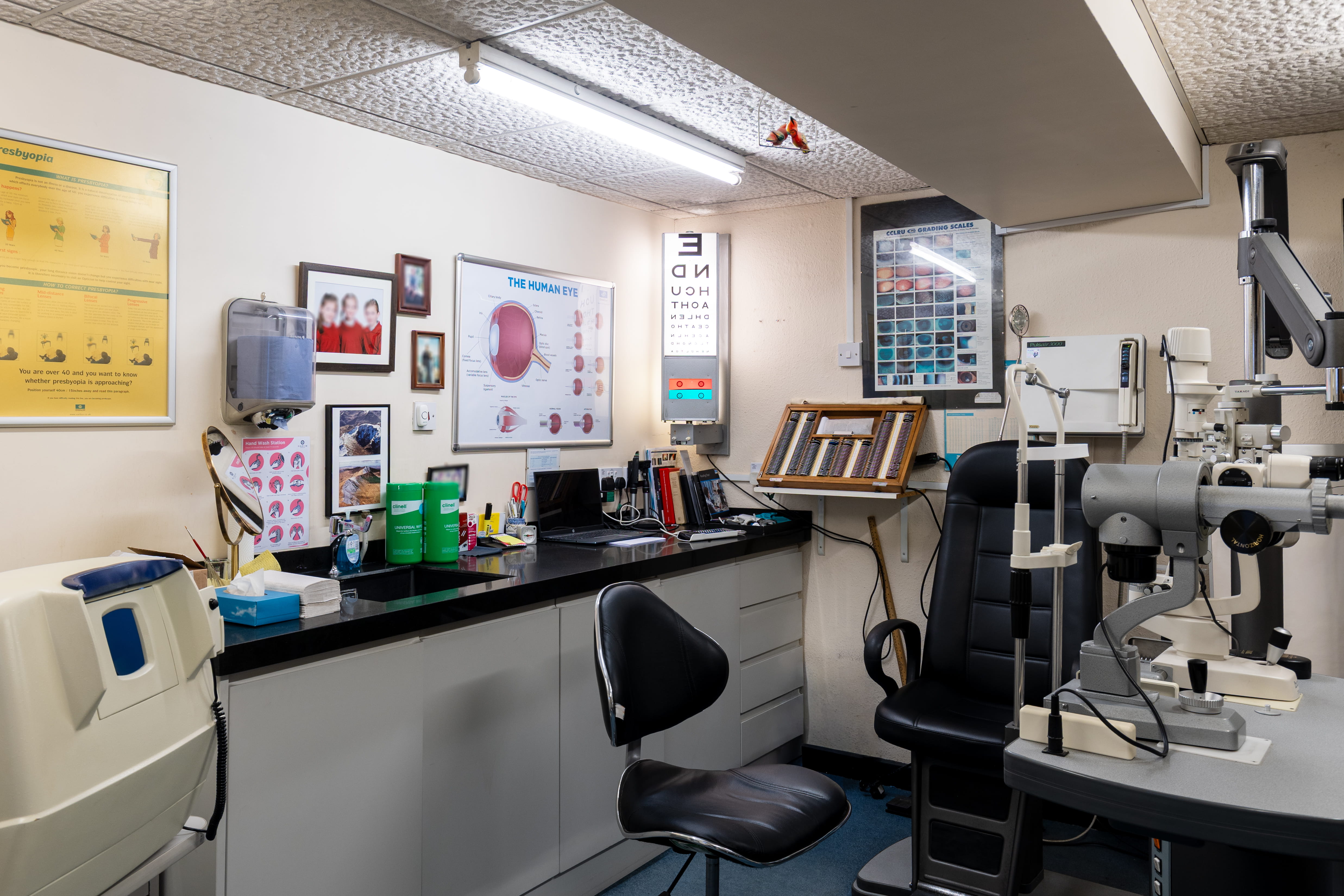 Interior of an eye exam room with testing equipment, charts, chairs, and medical supplies.