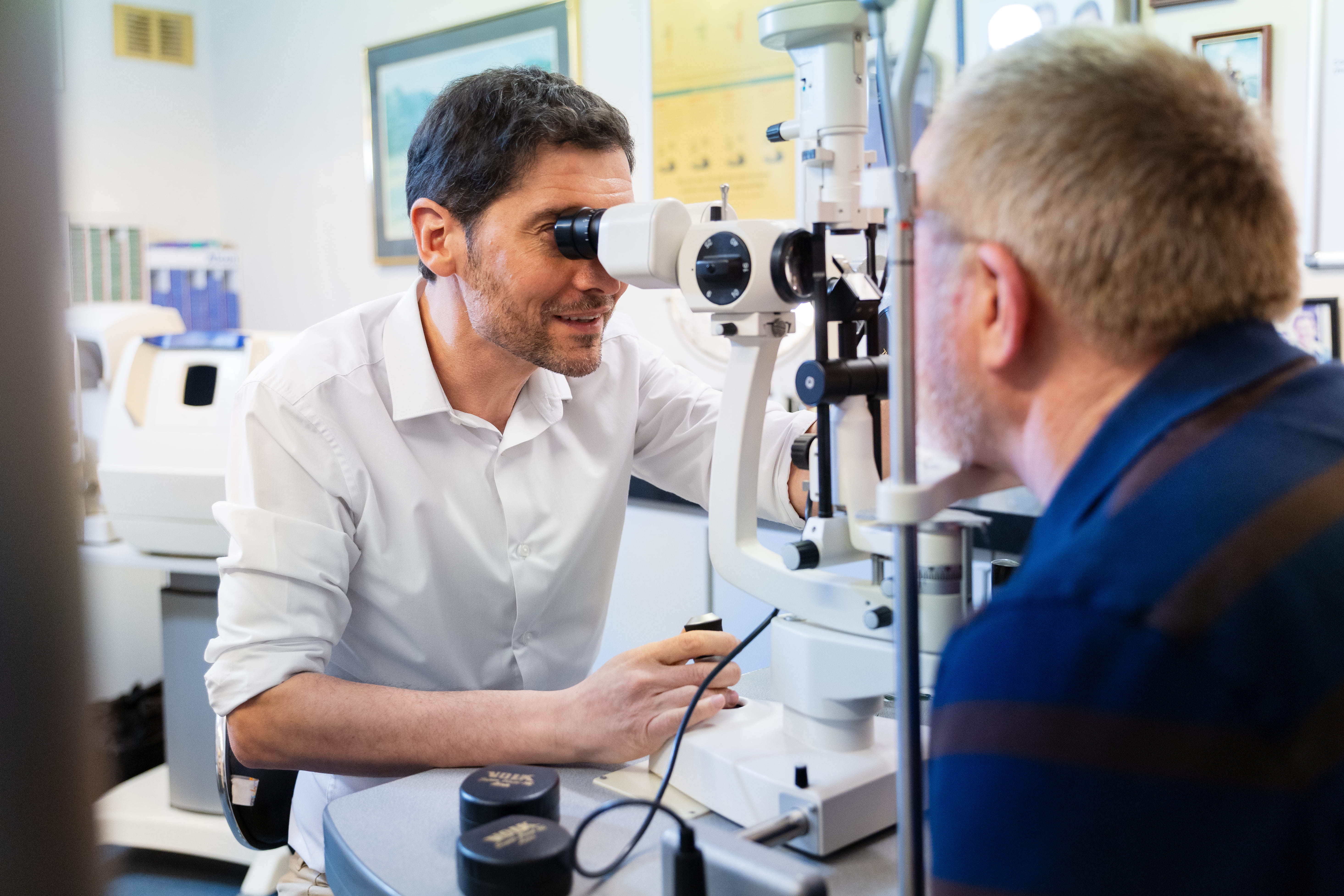 Optometrist using slit lamp to examine an older male patient's eyes in an eye clinic.