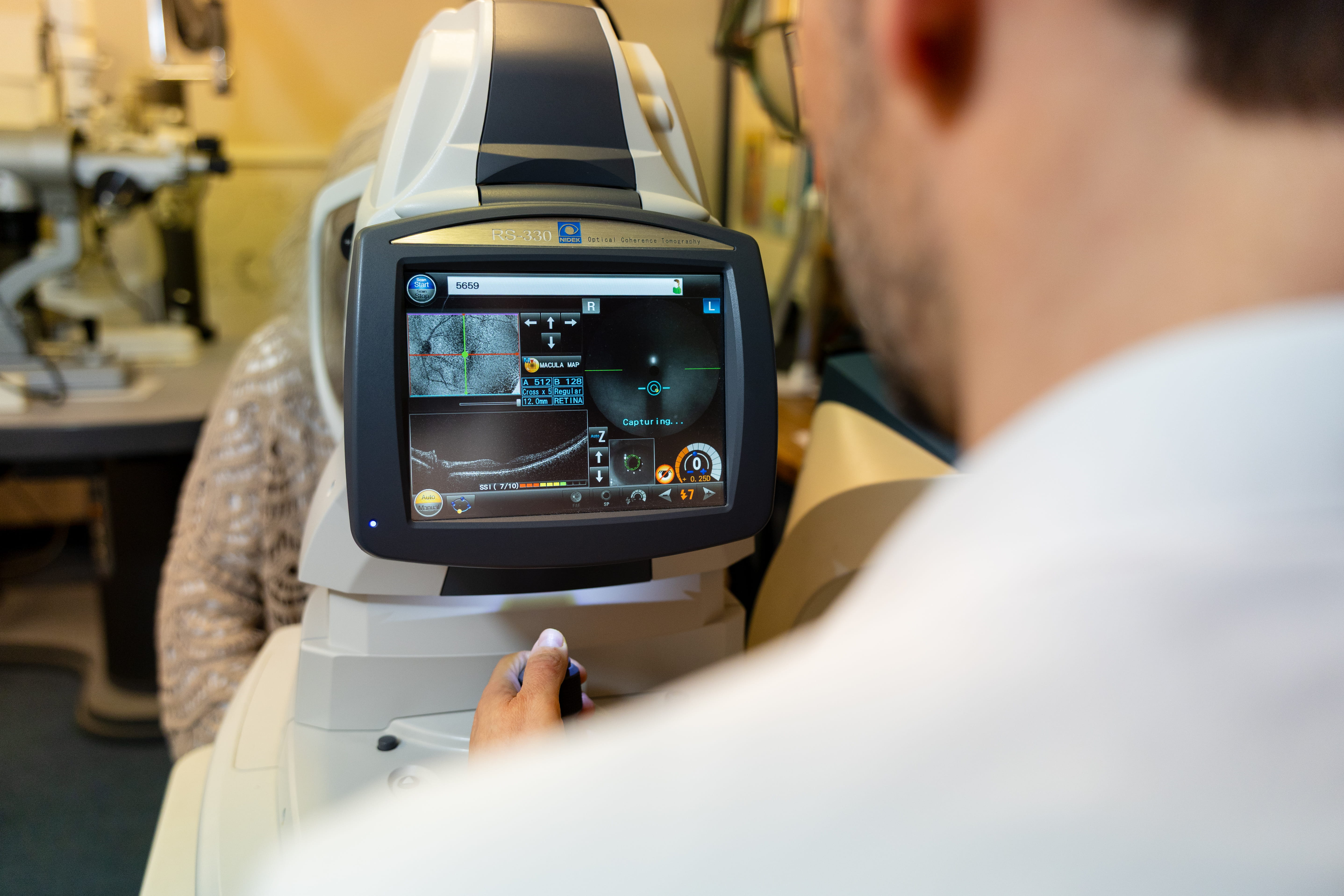 Eye exam machine screen showing retina scan while technician operates the equipment.