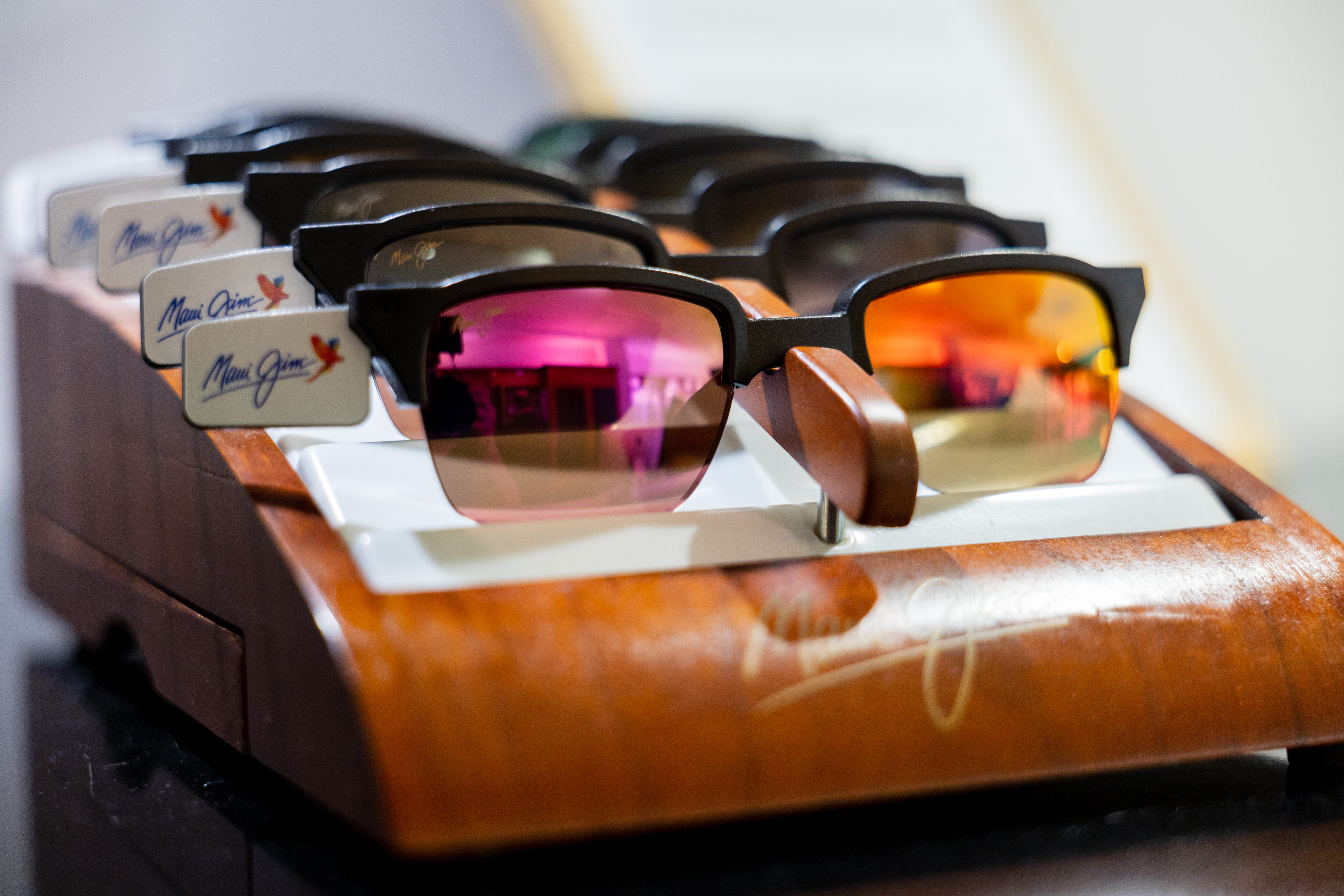 Multiple pairs of Maui Jim sunglasses with colored lenses displayed on a wooden rack.