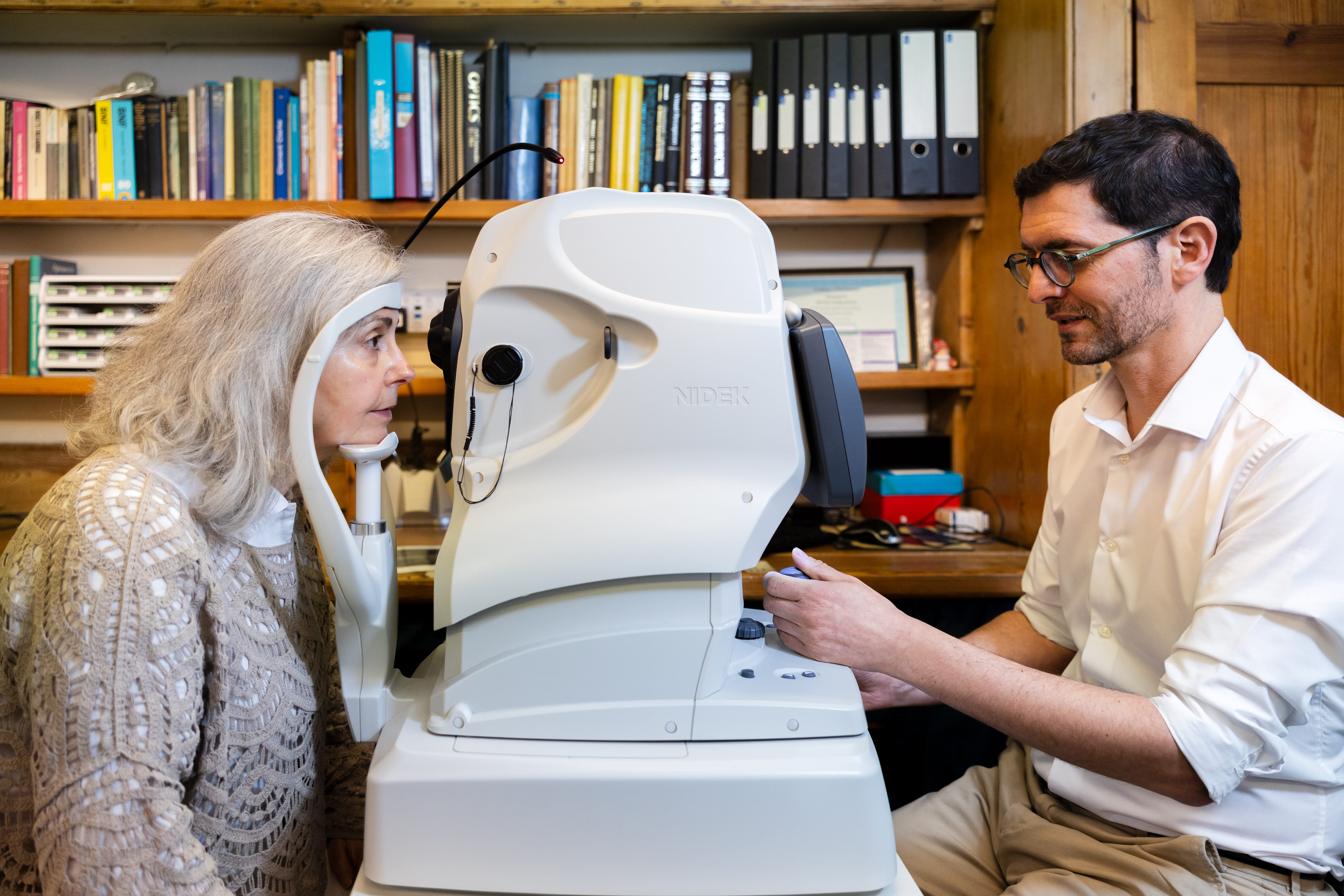 Older woman undergoing an eye test with optometrist using a NIDEK eye exam machine.