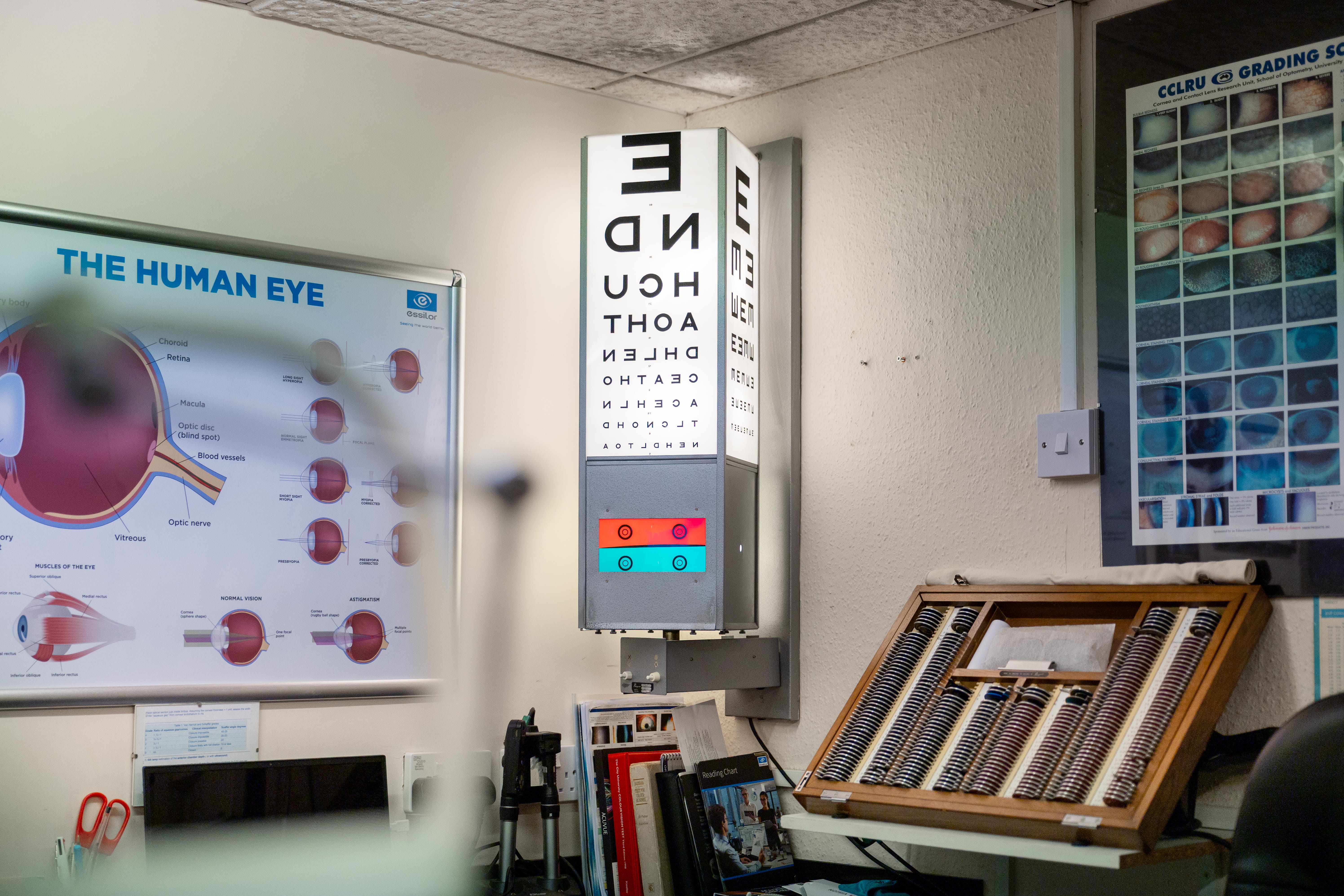 Eye clinic room with eye chart, posters on human eye and contact lens grading, and lens samples