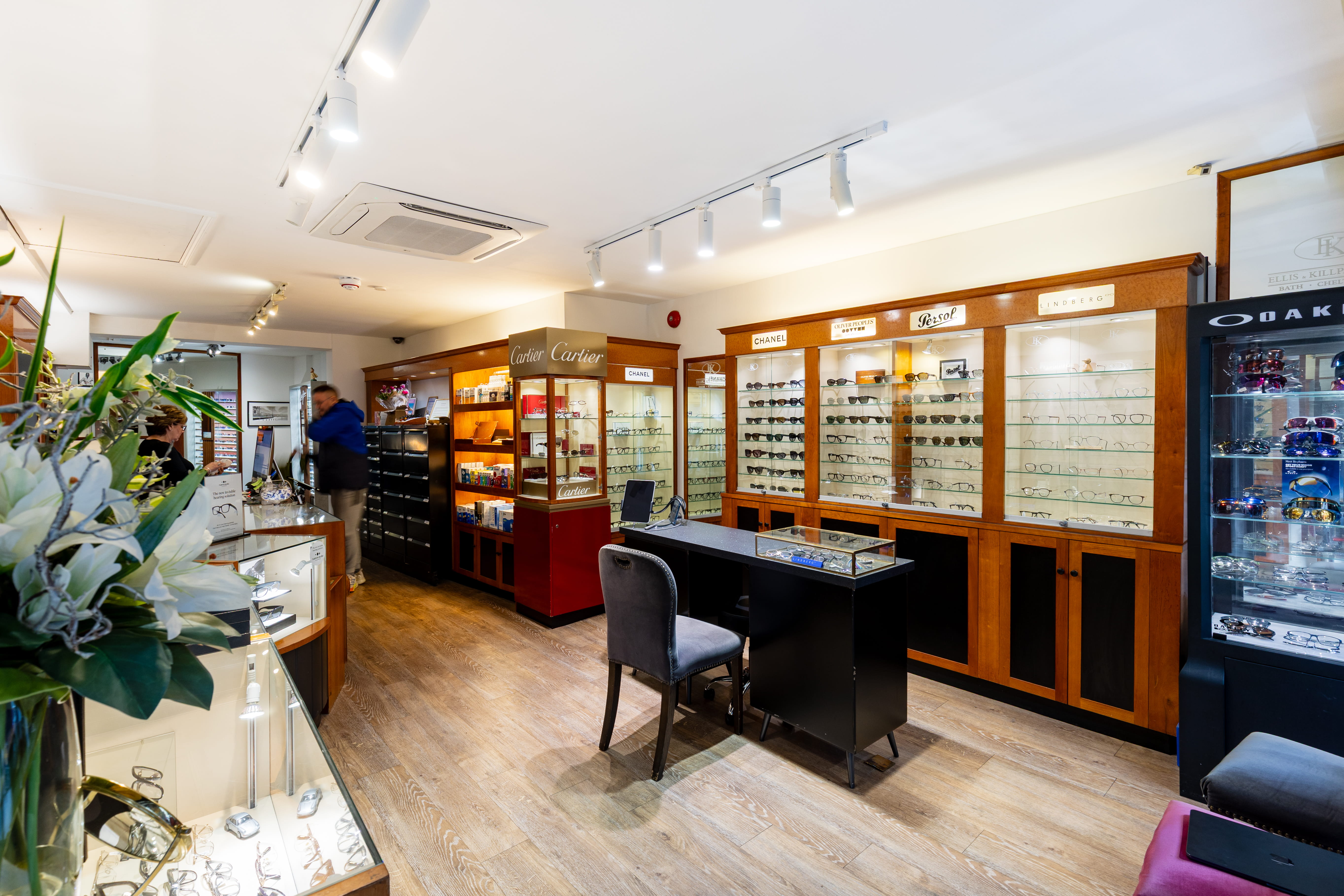 Interior of an eyewear store with wooden display cases filled with glasses and a consultation desk with a chair.