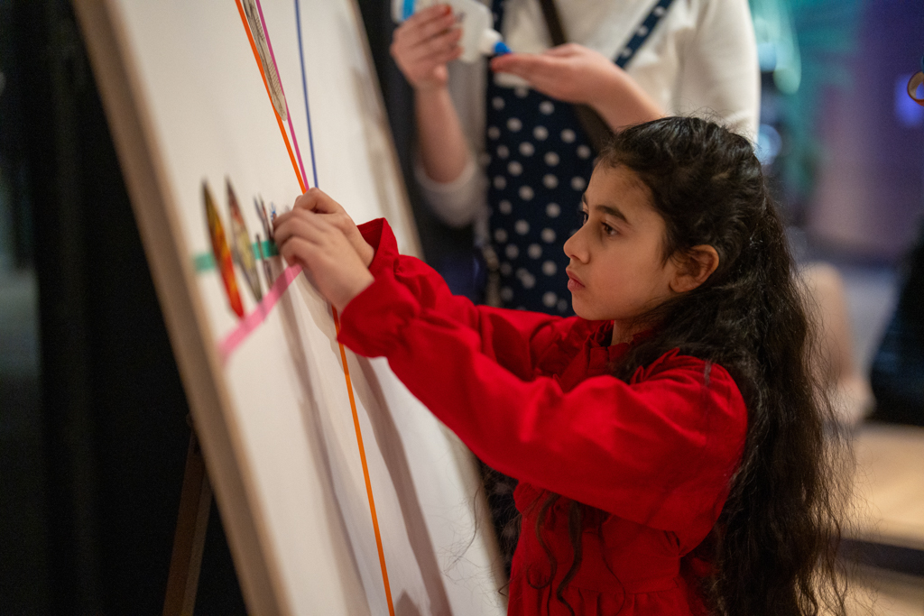 Foto van meisje die iets toevoegt aan het gezamenlijke kunstwerk van Dynamic Arts tijdens Nachtblik in Singer Laren