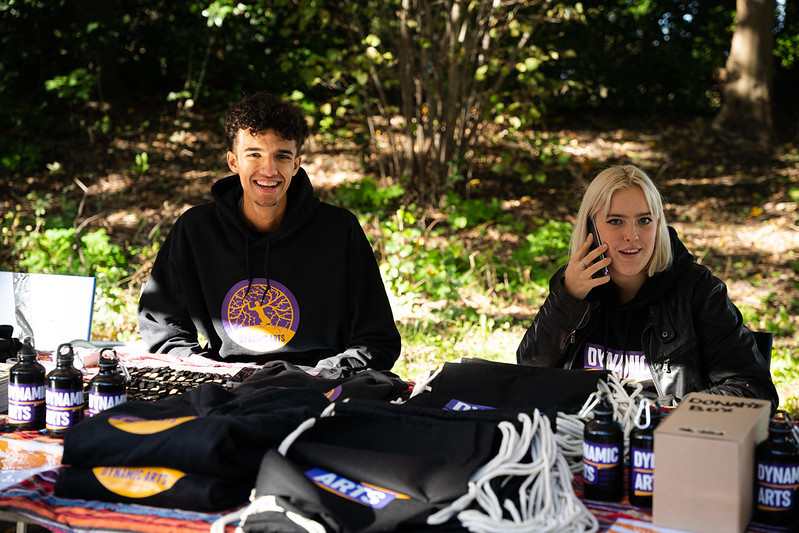 foto van twee Dynamic Arts stagiaires die achter een merchandise tafel zitten bij ons Beatstars festival