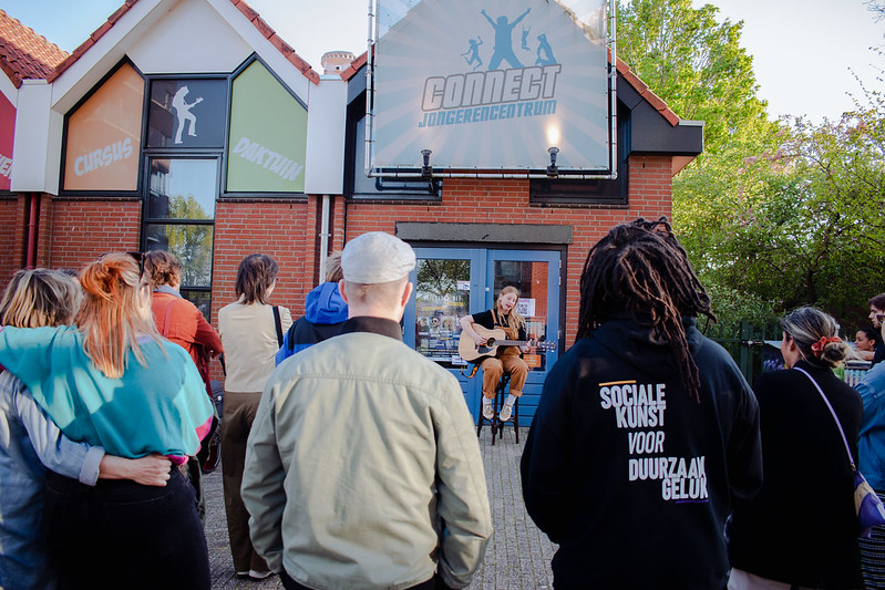 Foto van een meisje die zingt en gitaar speelt met publiek bij een Dynamic Arts show bij Jongerencentrum Connect in Huizen. 