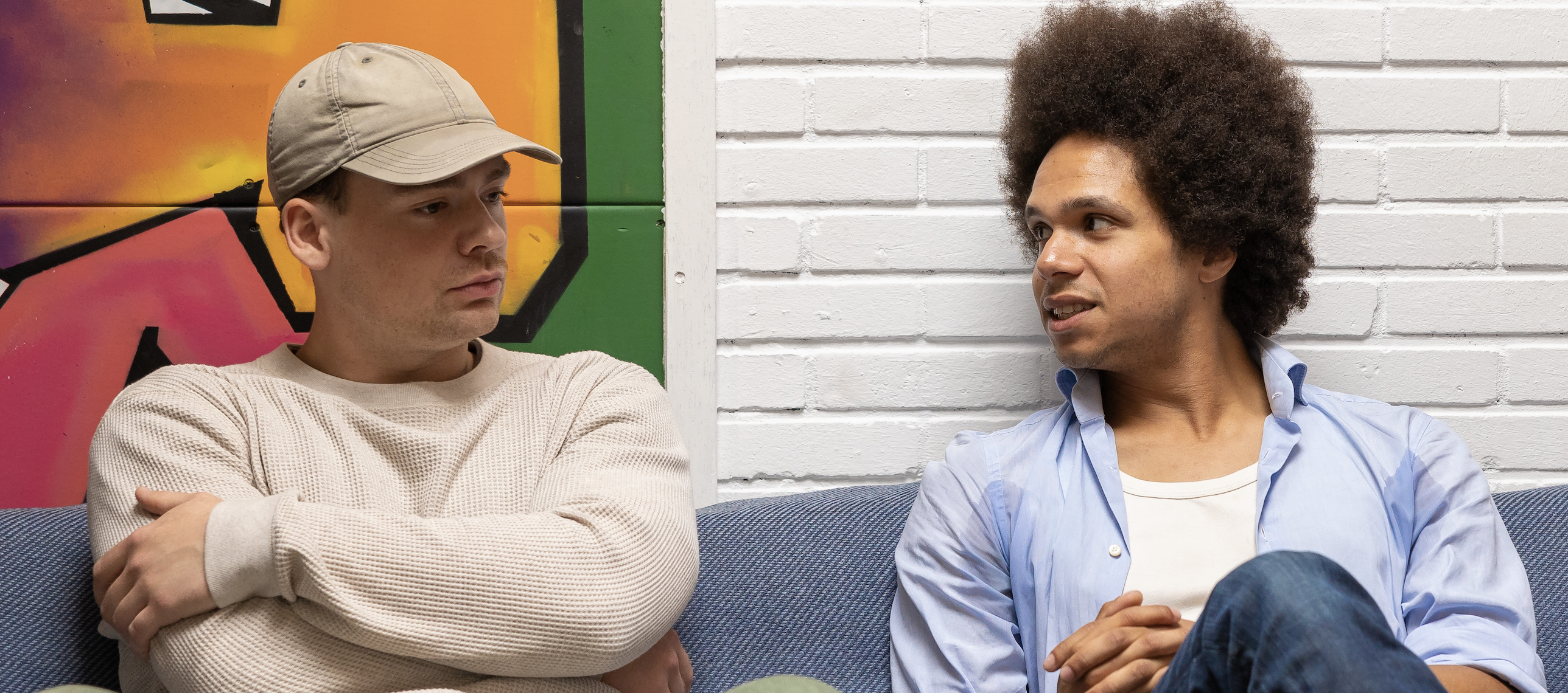 Twee jonge mannen op de bank bij Dynamic Arts in Laren in gesprek met graffiti op de achtergrond.