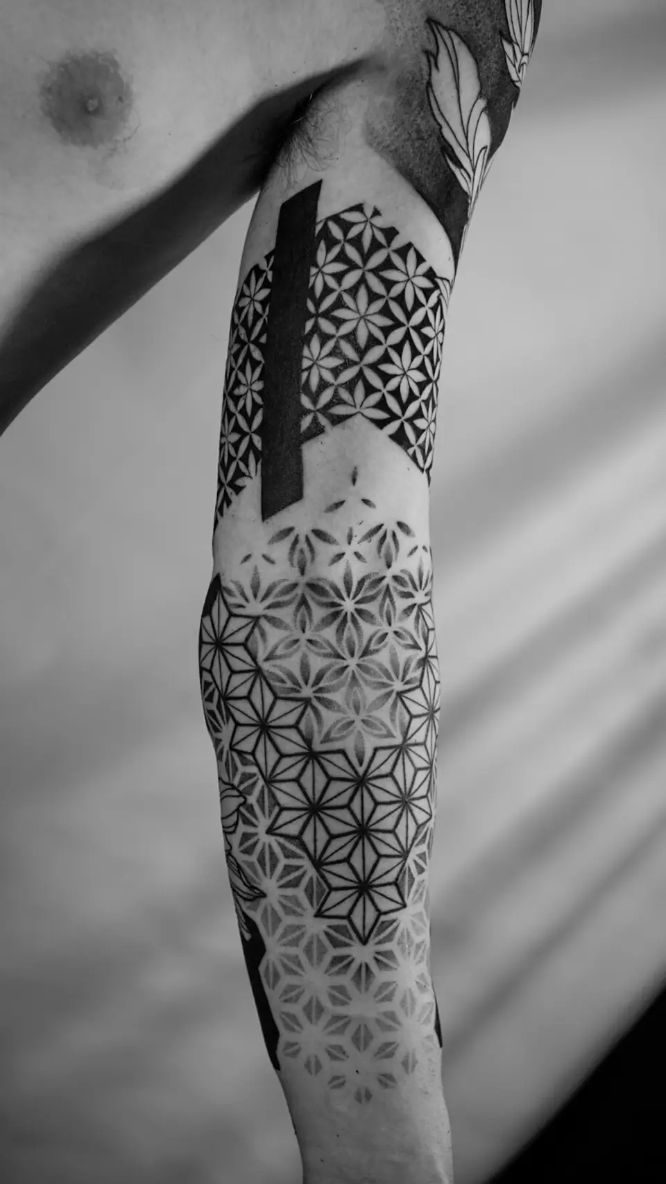 Black and white geometric patterned tattoo covering a person's upper arm from shoulder to elbow.